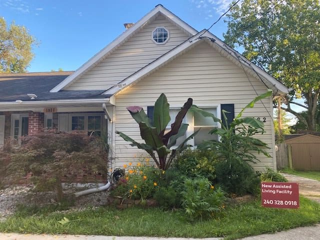 A cozy house with a lush garden and a 'for sale' sign in the front yard.
