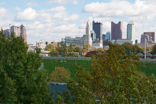 A scenic view of a city skyline framed by greenery and clouds, showcasing a blend of nature and urban architecture.