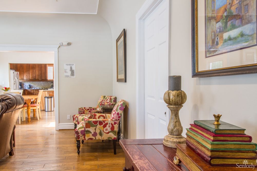 A cozy hallway featuring floral upholstered chairs, framed artwork on the walls, and a wooden console table with books.