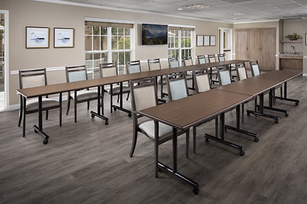 A modern conference room setup with long tables and chairs, featuring a television and large windows.