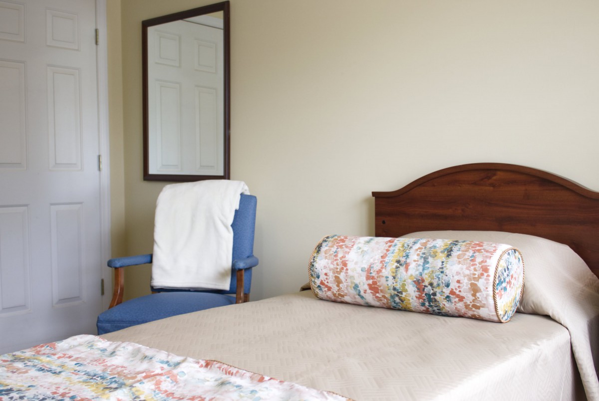 A cozy bedroom with a bed, chair, and mirror.