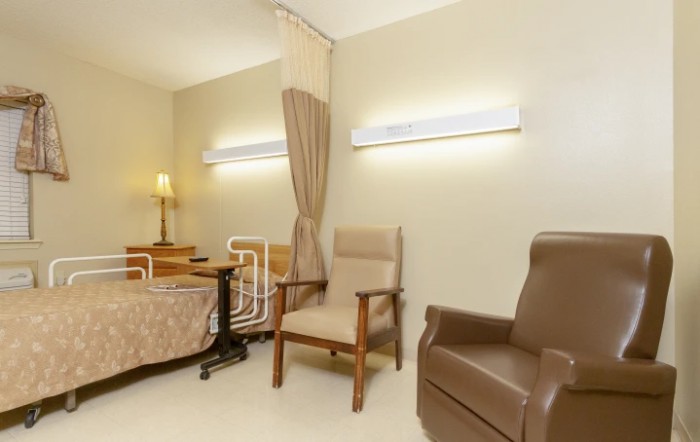 A well-furnished hospital room with a patient bed, comfortable chairs, and soft lighting.