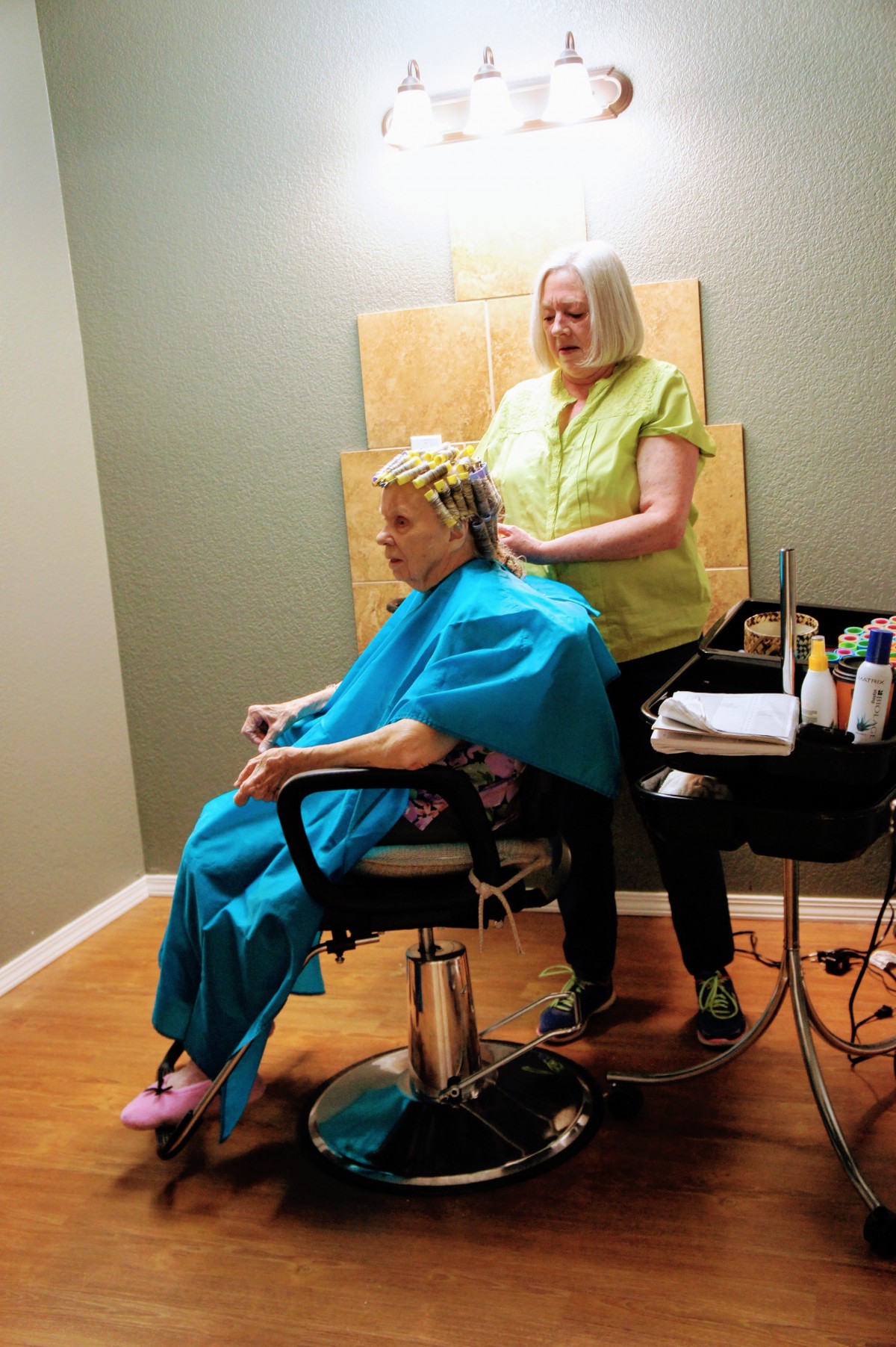 A hairdresser styles a senior's hair in a salon setting.