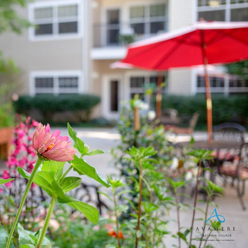 A peaceful outdoor patio featuring vibrant flowers and a red umbrella in an apartment setting.