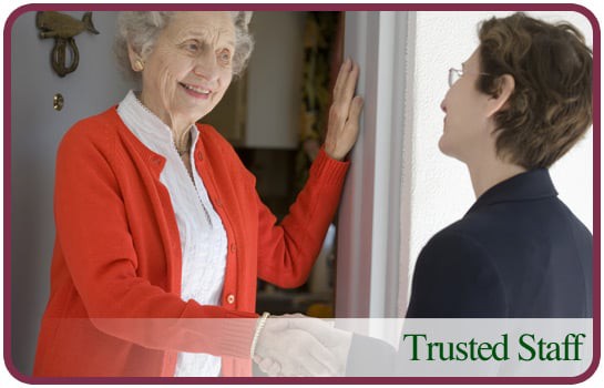 An elderly woman greeting another person at the doorway with a handshake.