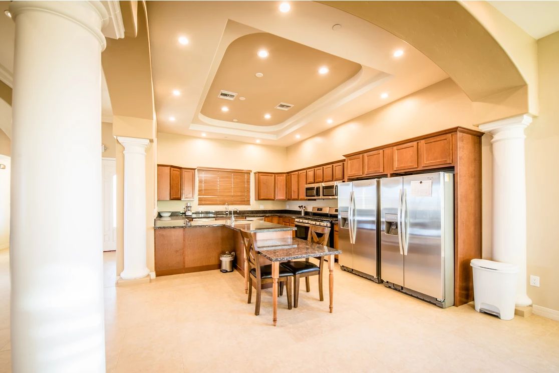A spacious and modern kitchen with wooden cabinetry, stainless steel appliances, and a dining area under recessed lighting.