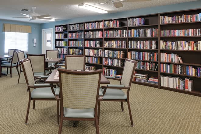 A quiet library room with bookshelves filled with books and a table with chairs arranged for reading or study.