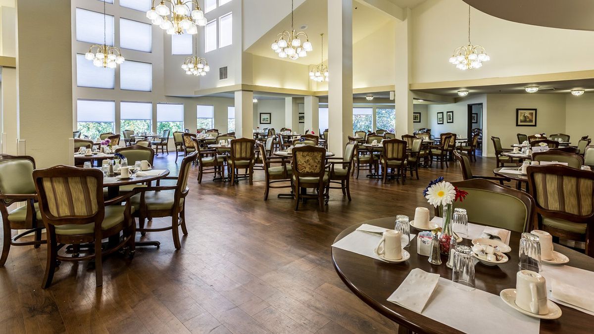 A spacious and elegantly decorated dining area with multiple tables and chairs, lit by chandeliers.