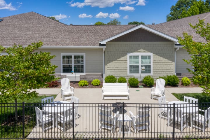 A sunny patio area with outdoor seating and a fenced yard in front of a residential house.