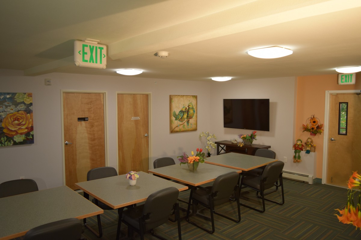 A well-lit conference room with tables, chairs, a television, and artwork on the walls.