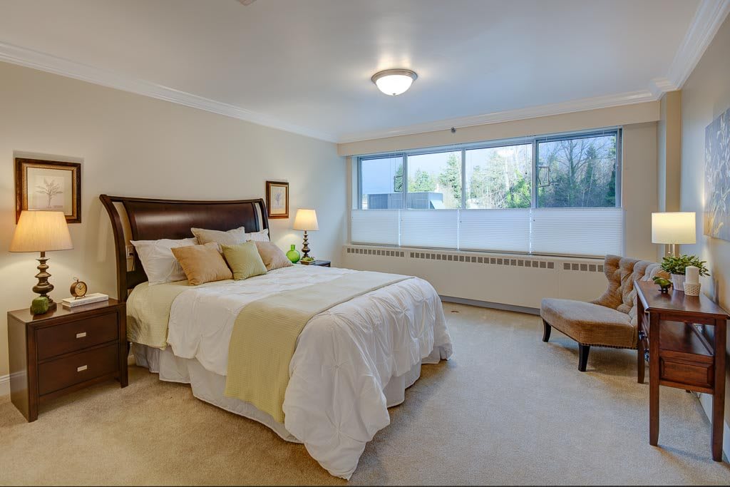 A cozy bedroom with a neatly made bed and large windows letting in natural light.