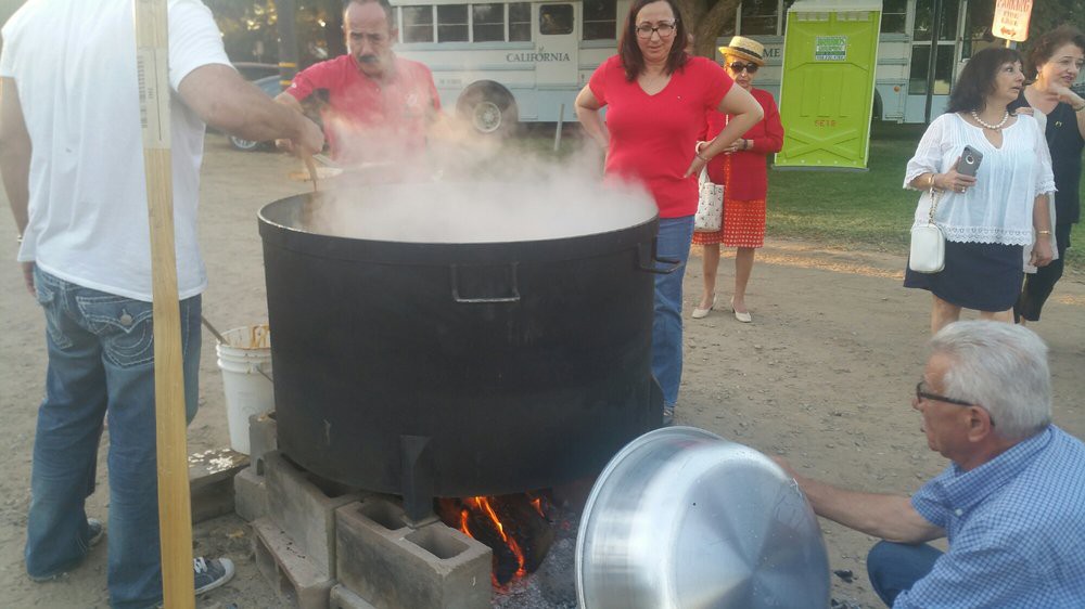 People cooking in a large pot outdoors at a festival.