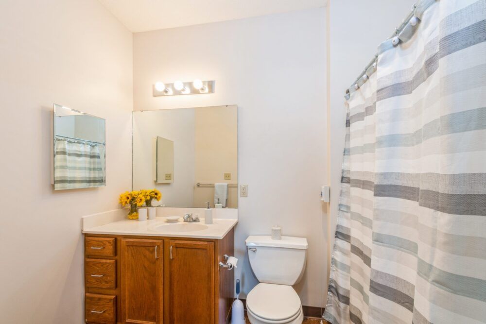A clean and modern bathroom with wooden cabinets, a large mirror, and a striped shower curtain.