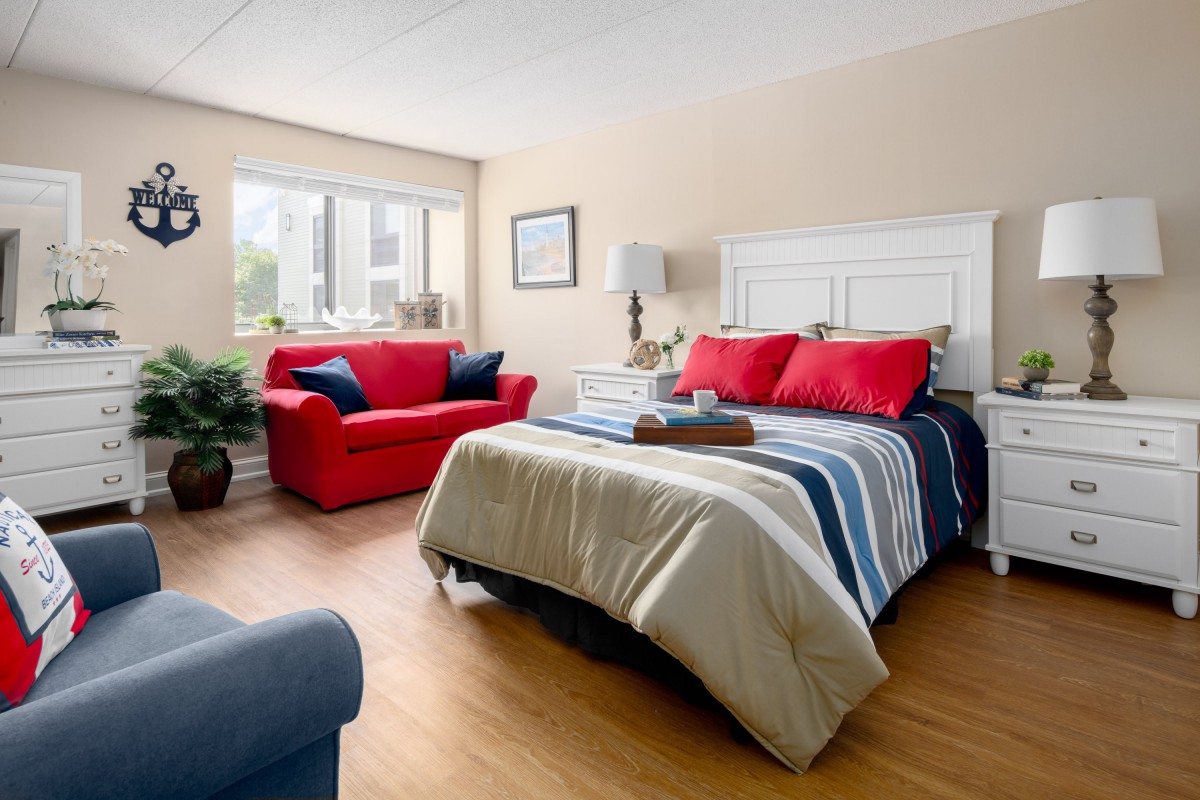 A cozy bedroom with a red and blue color scheme, featuring a comfortable bed and ample natural light.