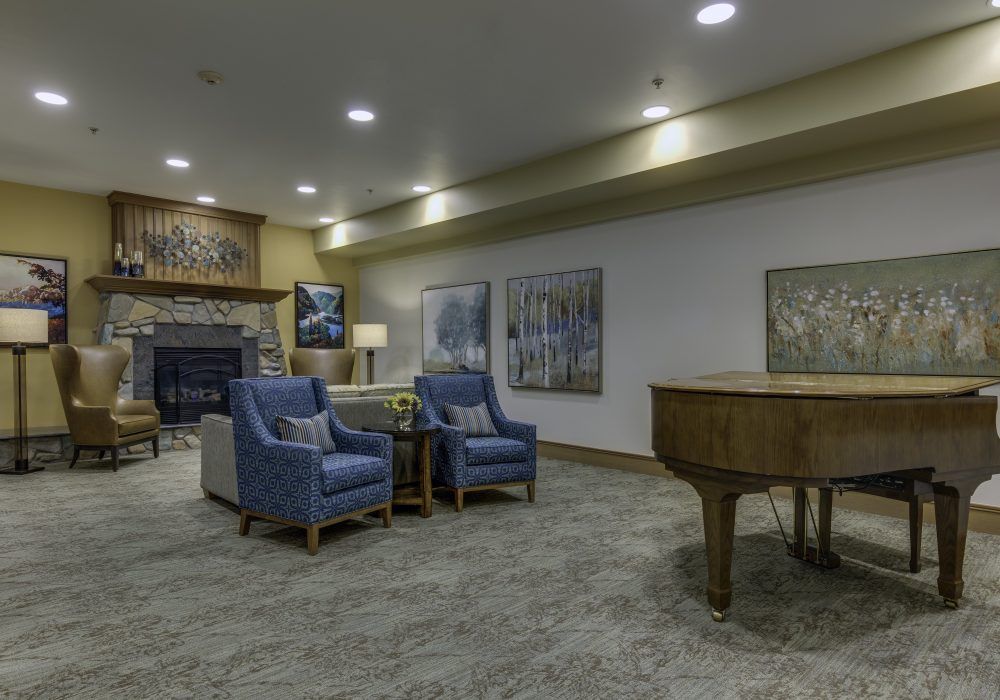 A cozy living room featuring armchairs, a grand piano, a fireplace, and decorative artwork.
