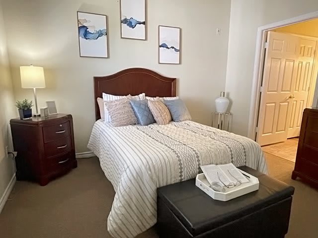 A cozy bedroom with a neatly made bed, decorated with pillows and artwork on the walls.