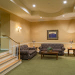 A cozy living room area featuring a sofa set, wooden table, and decorative lighting, with stairs leading to another level.