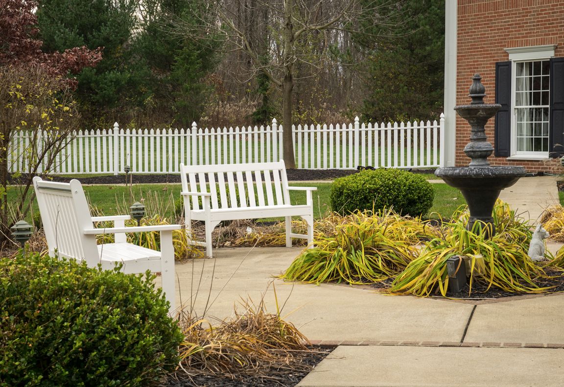 A serene garden patio with white benches and lush greenery.