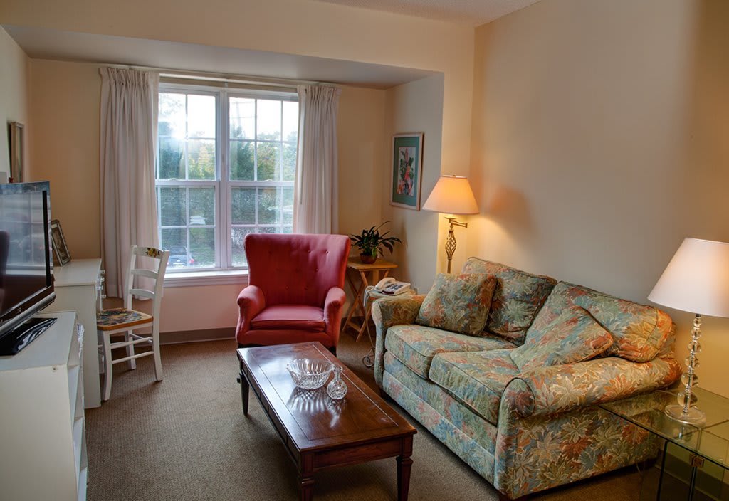 A cozy living room with a floral-patterned sofa and a red armchair near a window.