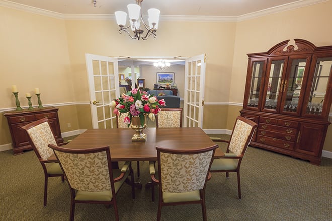 A dining room featuring a wooden table with decorative chairs, a floral centerpiece, and elegant lighting.