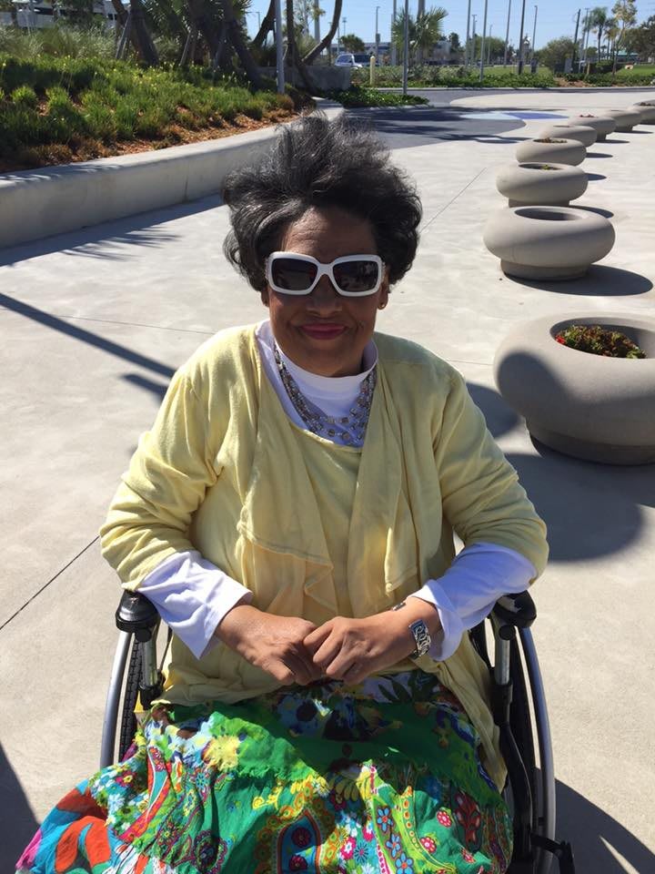 A woman in a wheelchair wearing sunglasses enjoys a sunny day outdoors.