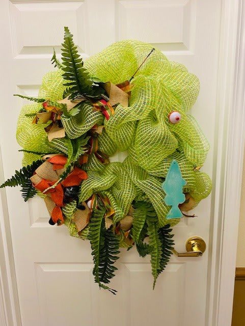 A vibrant tropical-themed wreath with green mesh, ferns, and colorful accents adorns a white door.