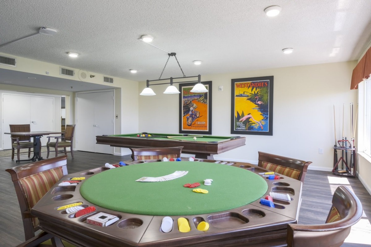 A well-lit game room featuring a round poker table with green felt and colorful chips, adorned with decorative posters on the walls.