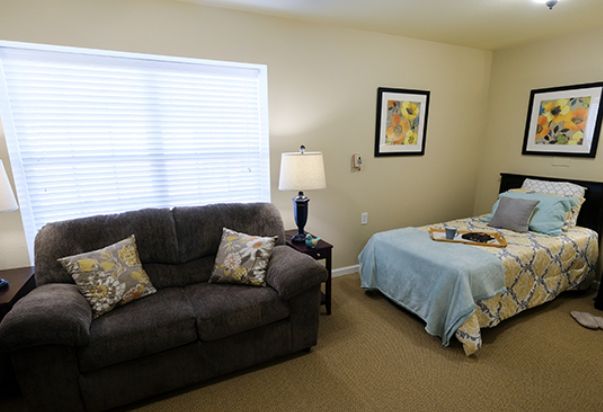A cozy room featuring a sofa and a bed with a lamp by the window.