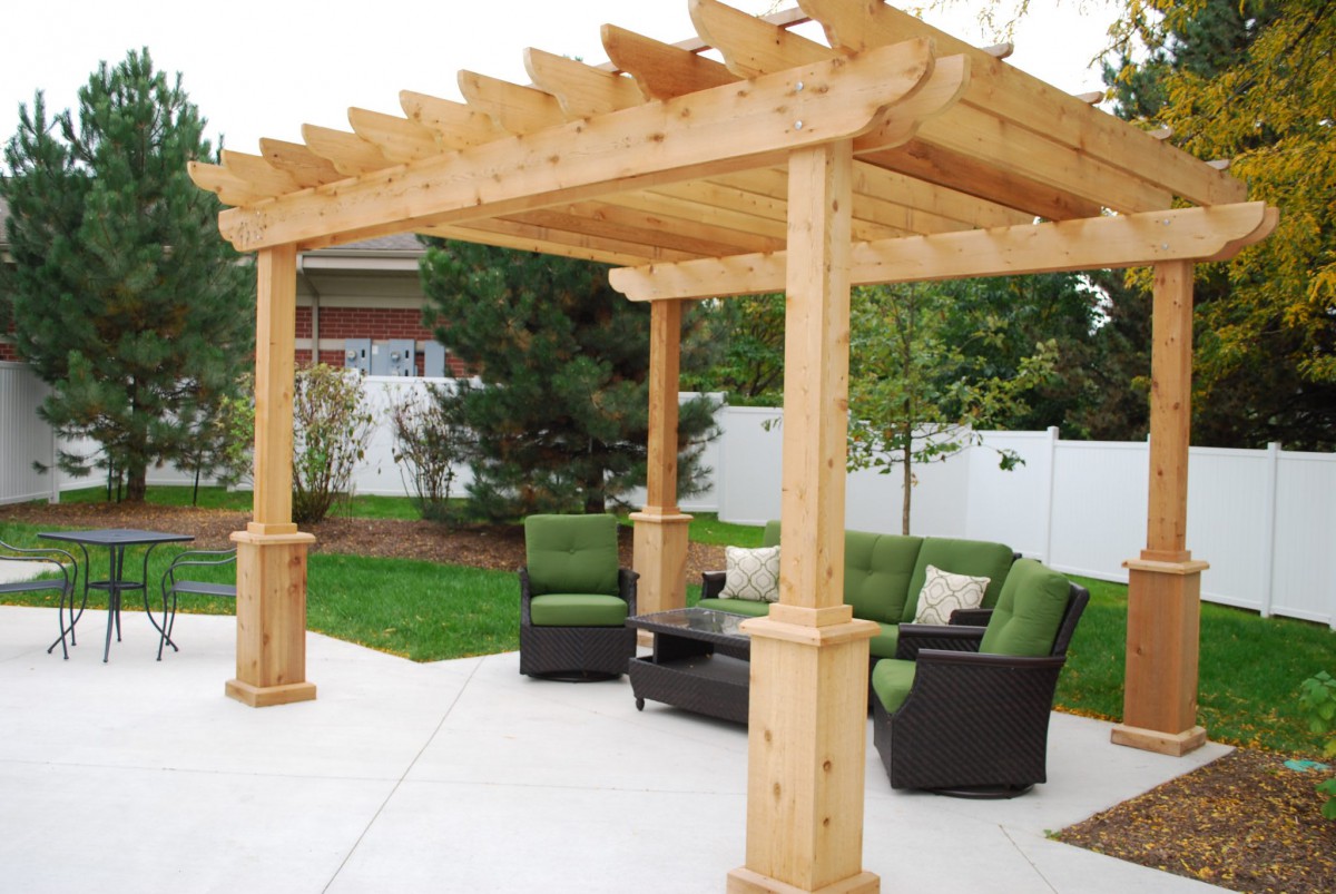 A wooden pergola with outdoor seating in a backyard setting.