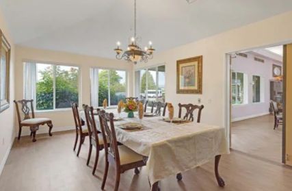 A bright and elegant dining room with a chandelier, table, and chairs, complemented by large windows.