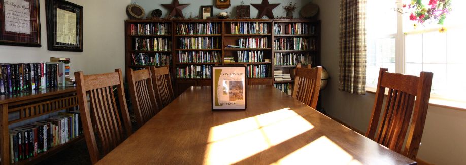Sunlit library room with a table and bookshelves.