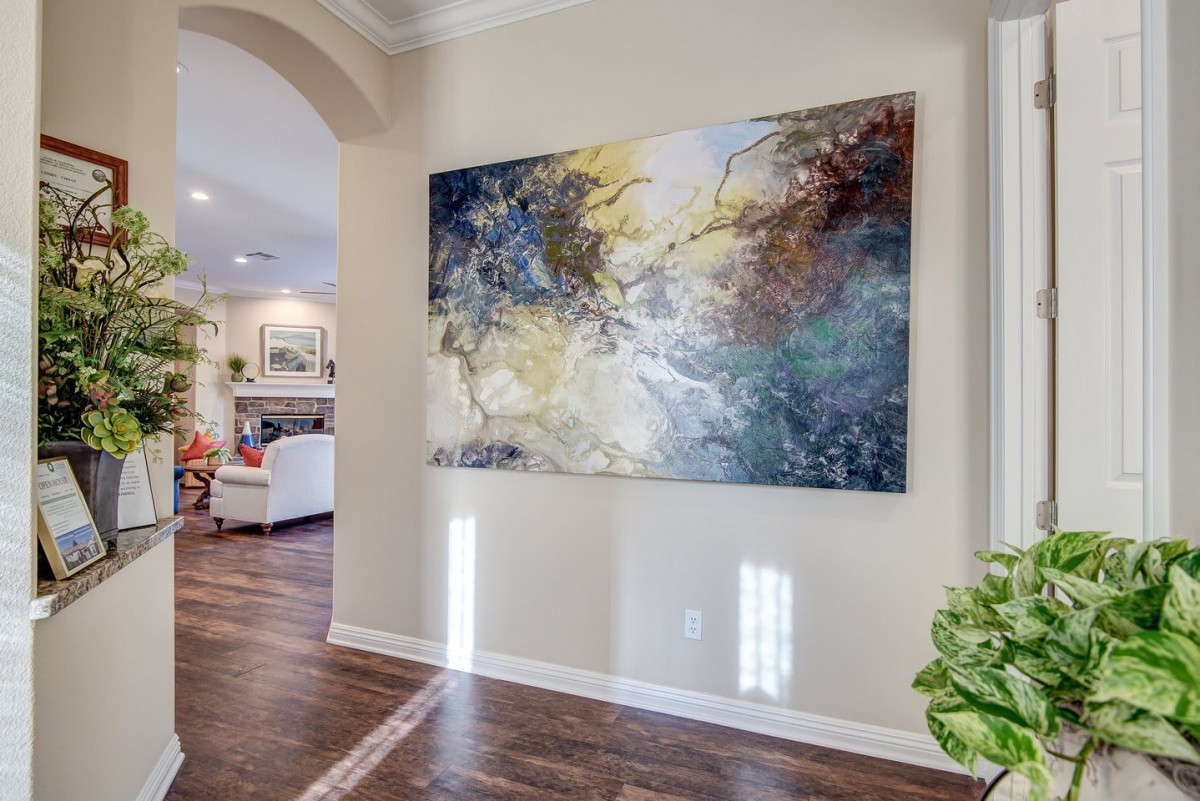 A modern home interior featuring a large abstract painting in the hallway, with a glimpse of the living room in the background.
