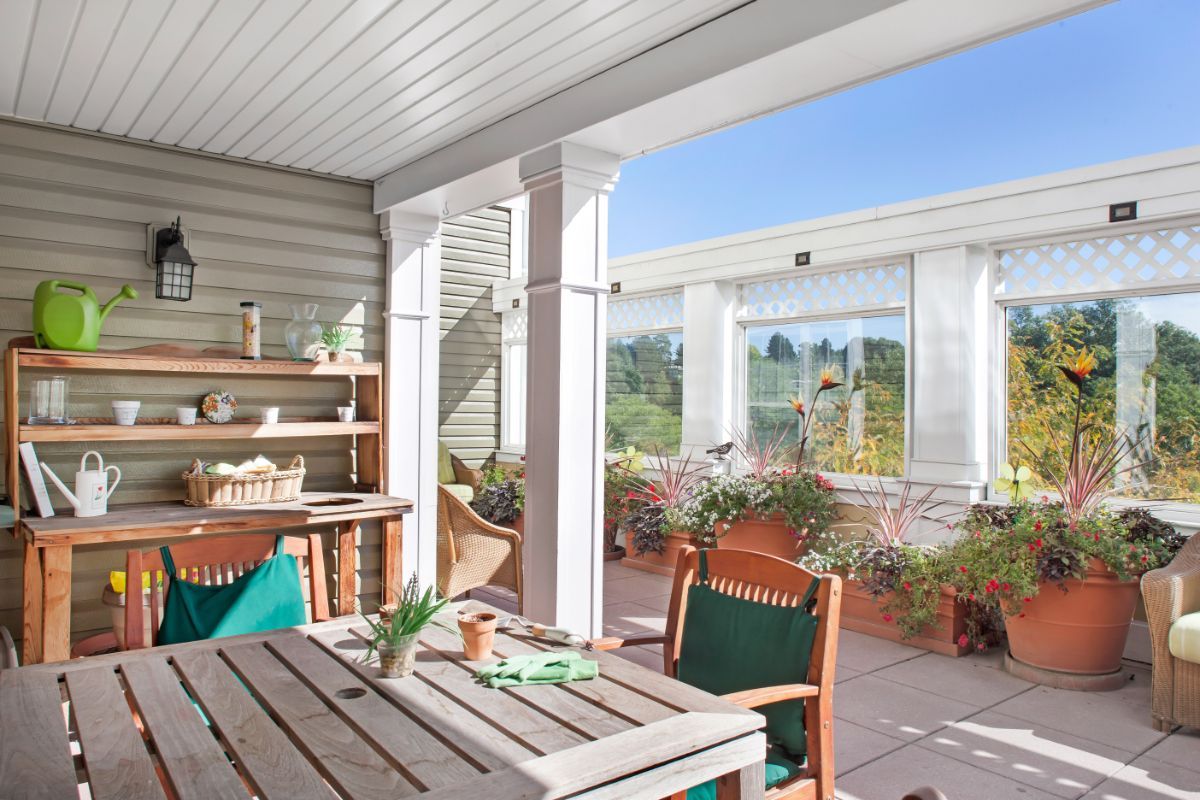 A cozy outdoor patio with wooden furniture, plants, and a sunny setting.