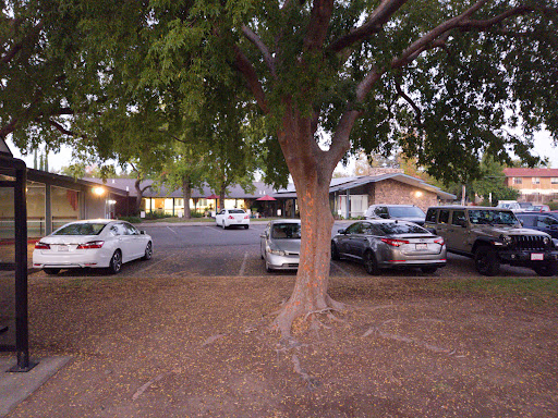 A view of a parking lot surrounded by trees, with several cars parked in a residential area during the evening.