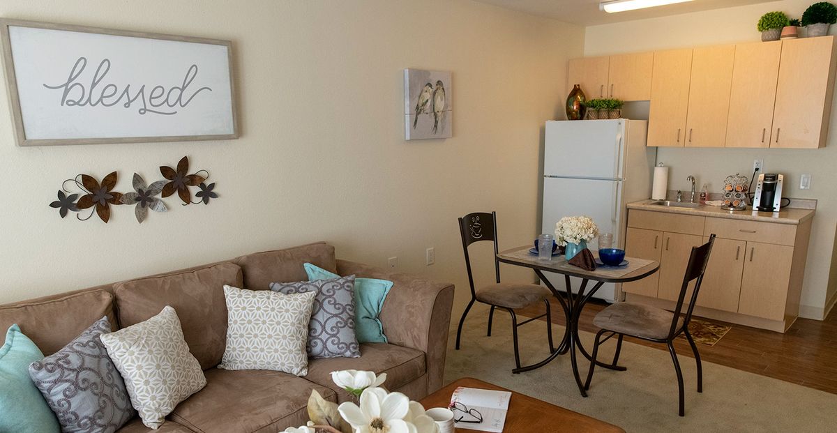 A cozy living room with a sofa, decorative pillows, and a dining table in front of the kitchen area.