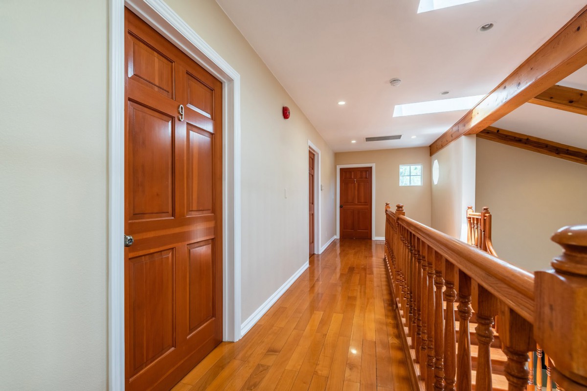 A hallway with polished wooden floors and doors, featuring a banister and recessed lighting.