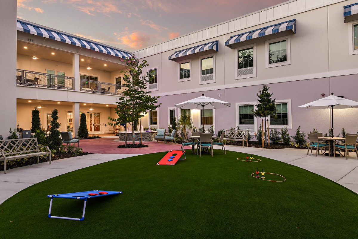 A courtyard with outdoor furniture and lawn games, set in front of a building at sunset.