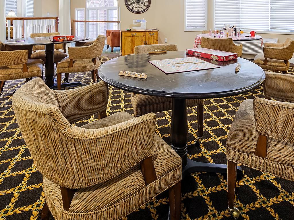 A cozy lounge area with a round table surrounded by upholstered chairs, a patterned carpet, and board games on the table.