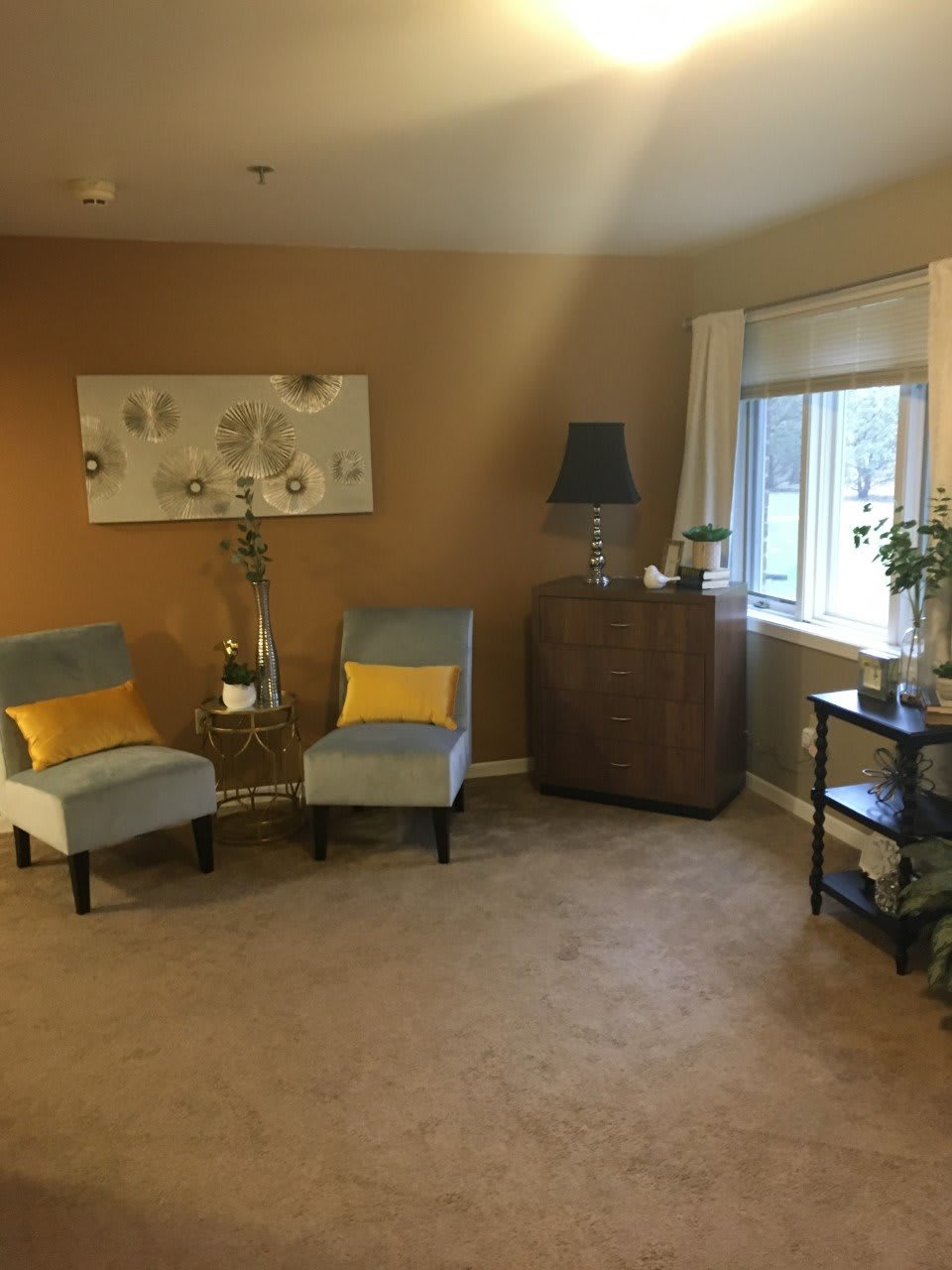 A cozy living room with neutral tones and yellow accents, featuring two chairs, a side table, and a window bringing in natural light.