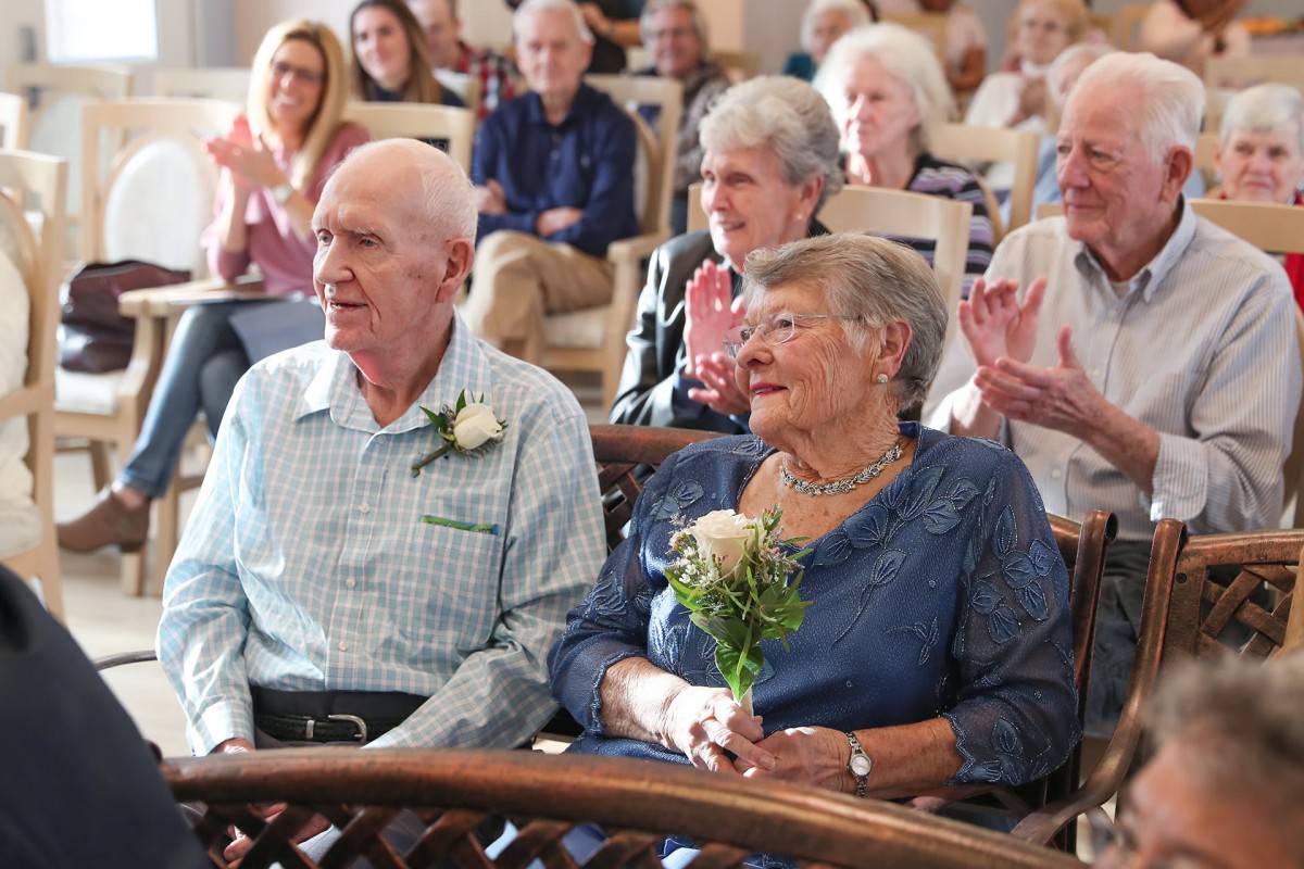 An elderly couple sitting in an audience, celebrating with flowers.