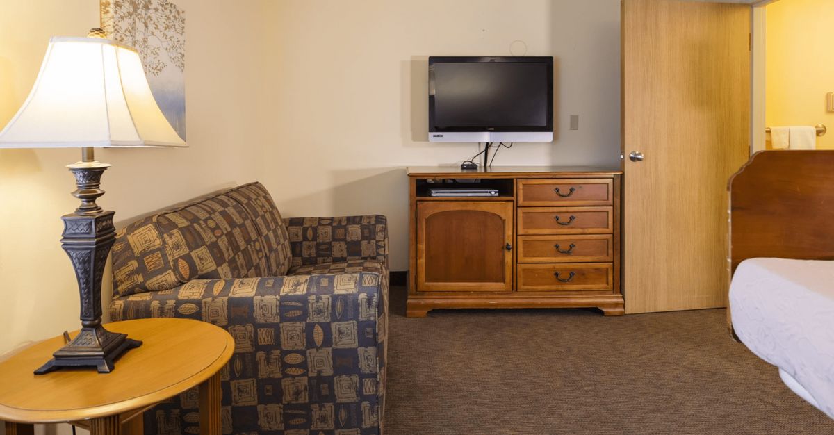 A cozy hotel room with a patterned couch, television, and wooden dresser.