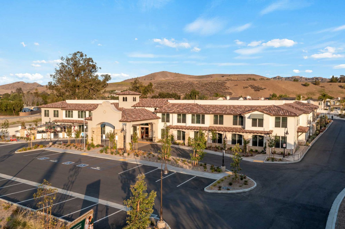 A modern building with a parking lot set against a scenic landscape and a clear blue sky.