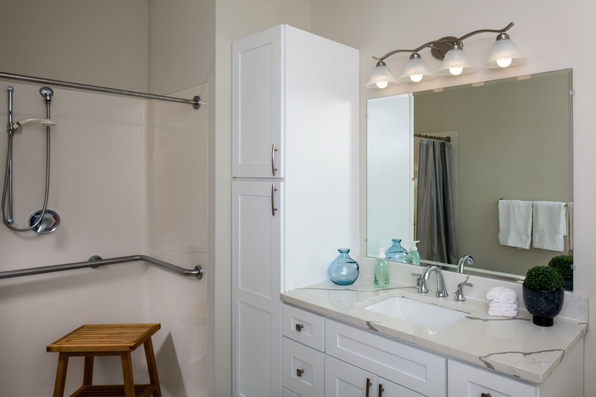 A well-lit bathroom with a white cabinet, decorative jars, and a large mirror above the sink.