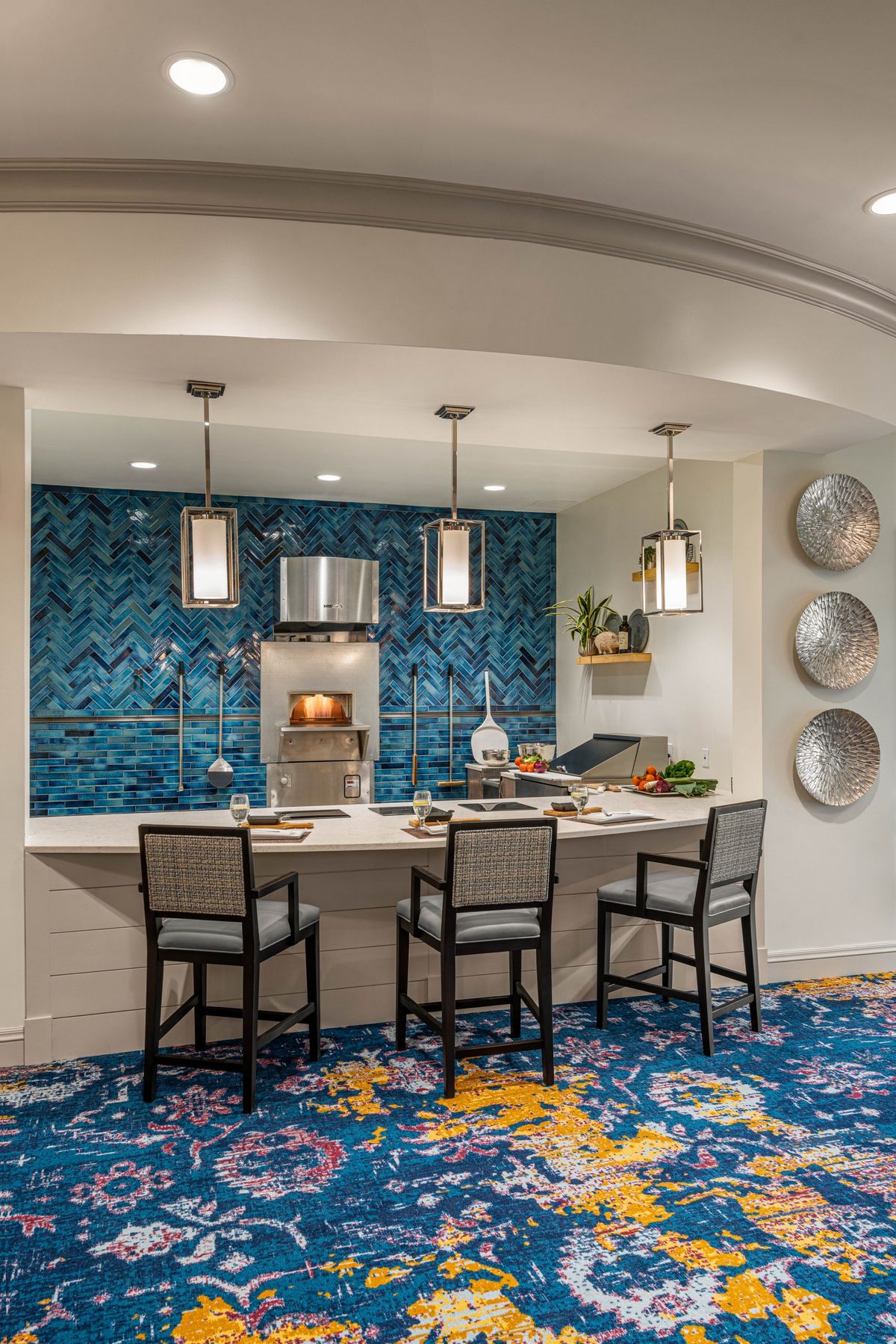 A modern kitchen with a blue mosaic backsplash, pendant lights, and bar seating.