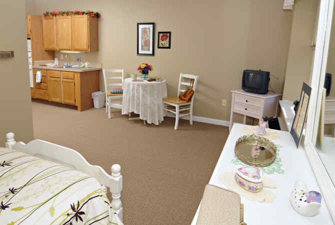A cozy bedroom with a small table and chairs, a TV on a stand, and a kitchenette area.