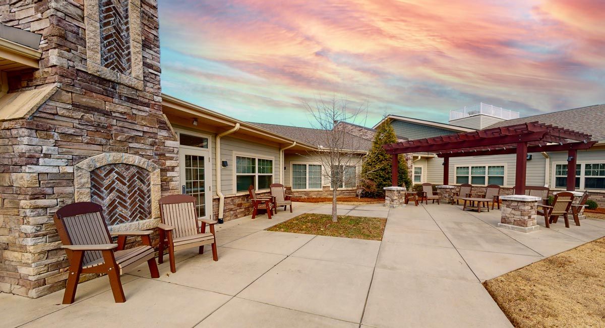 A peaceful courtyard with wooden chairs, surrounded by buildings, under a colorful sunset sky.