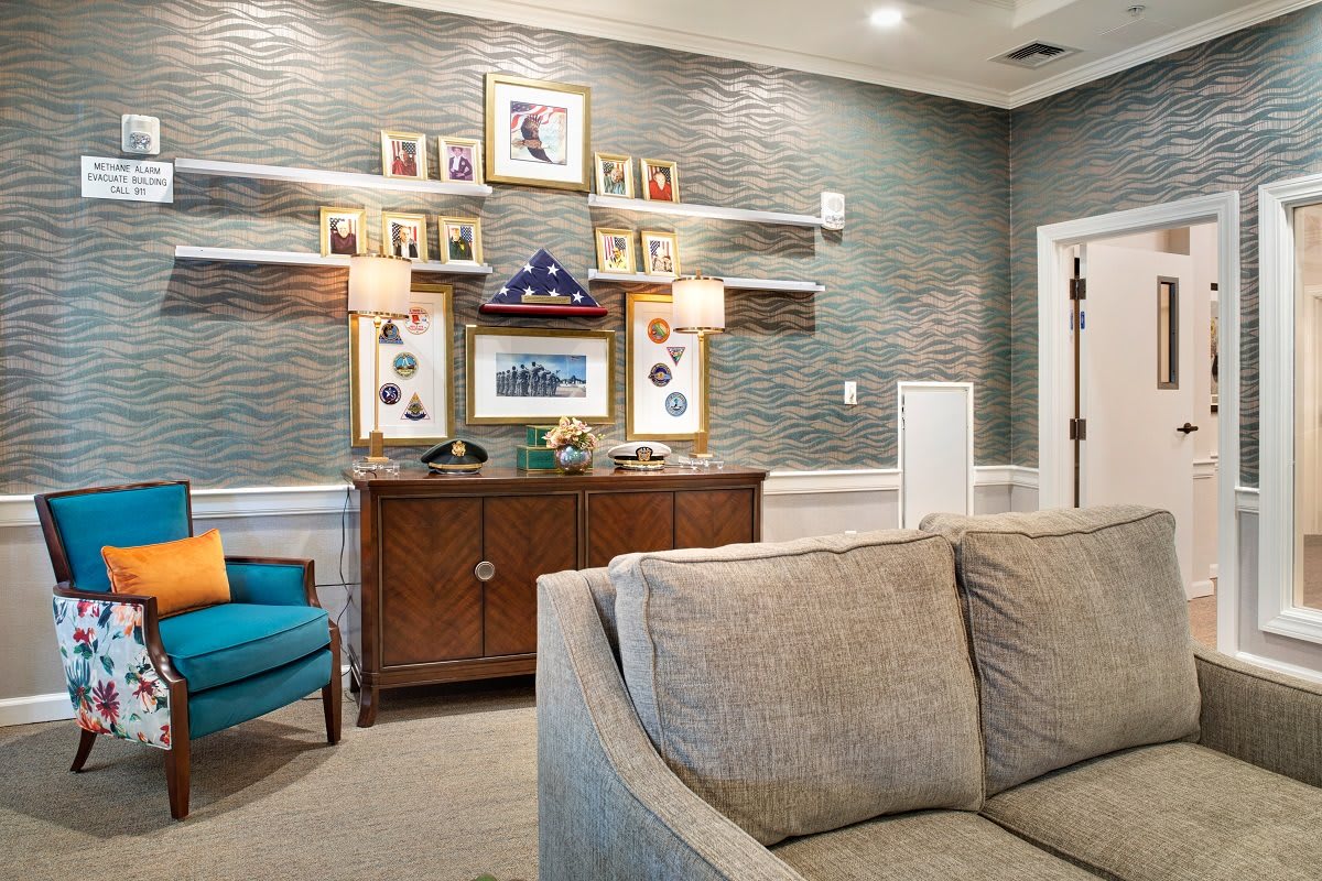 A cozy living room with a sofa, armchair, and a wooden cabinet adorned with pictures and lamps.