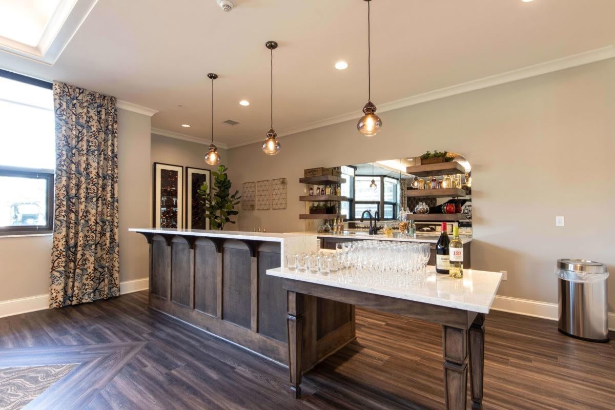 A modern home bar featuring pendant lights, wooden flooring, and elegant shelving with wine bottles.