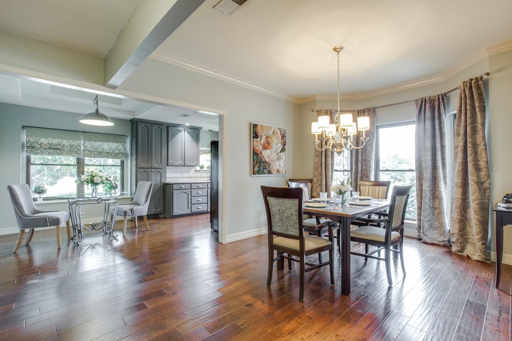 A spacious dining room with a view into the kitchen, featuring elegant wooden flooring and a chandelier.