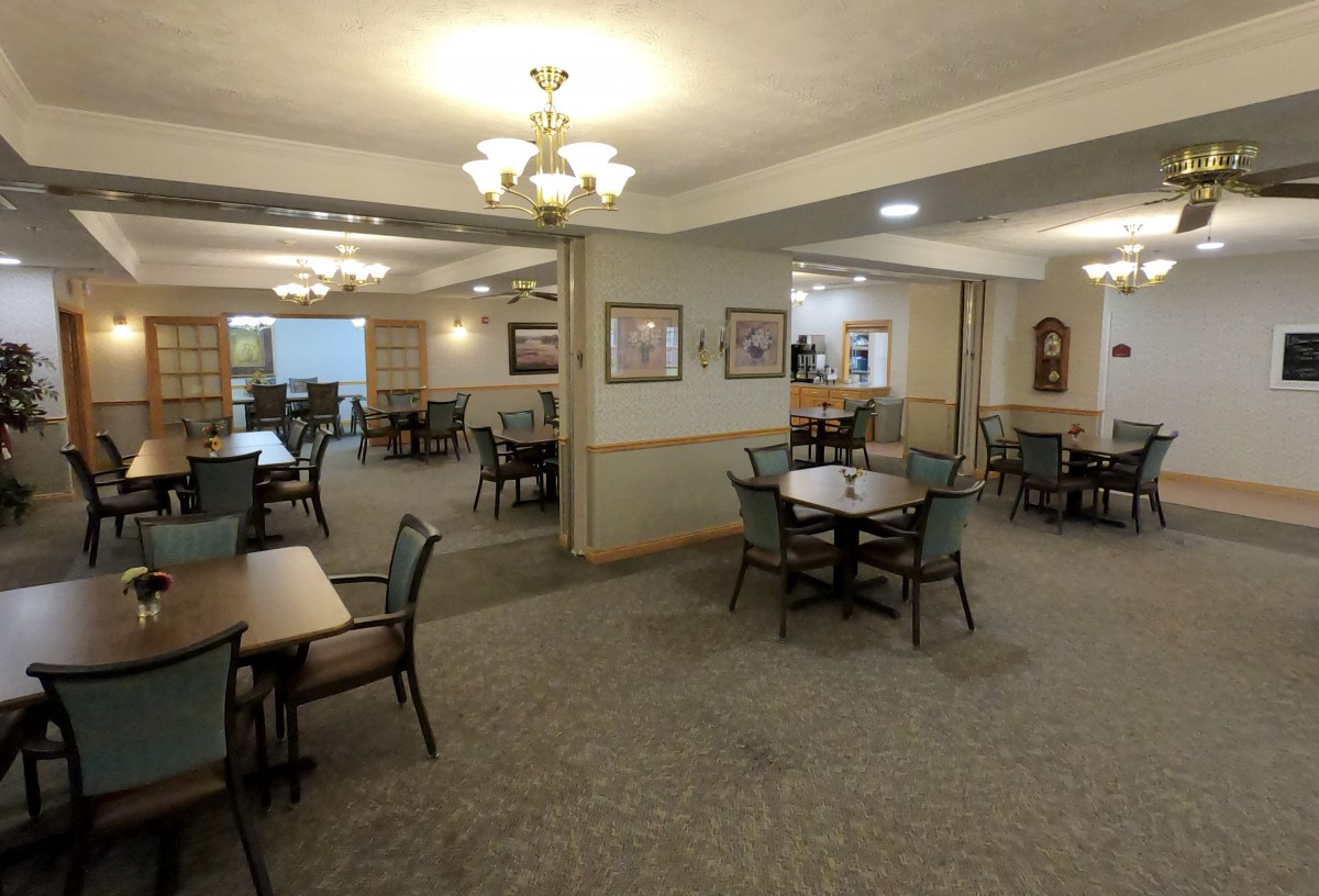 A spacious dining room with multiple tables and chairs, decorated with chandeliers and wall art.